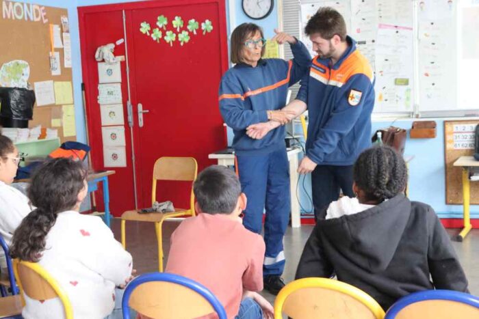 deux secouristes font une démonstration devant des enfants assis