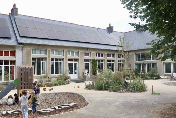 panneaux solaires sur la toiture d'une école, des enfants jouent dans la cour au premier plan